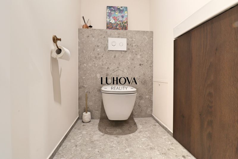A toilet with decorative art, gray tiles, and wooden decor in a 3-room apartment.