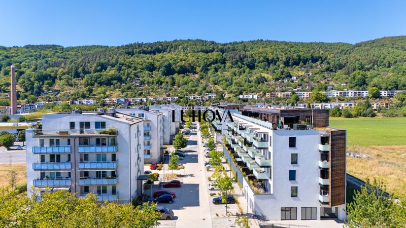 Púchov, Dlhé lúky: Row housing with apartments, green hills and greenery in the background.