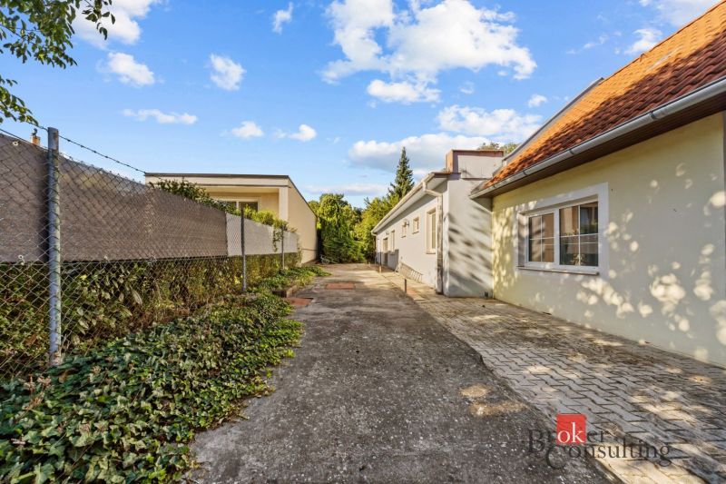 The exterior of a family house in Budmerice, a paved path surrounded by greenery and a fence.