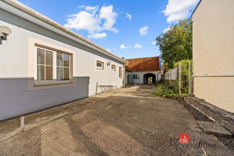 A family house in Budmerice with a paved courtyard, next to a fence with vegetation.