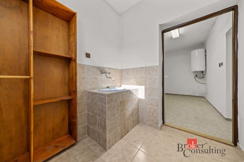 A kitchen area in a family house with a shelf and a sink, view into the utility room.