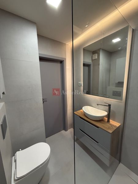 Bathroom in a studio apartment with a sink on a wooden decor and a built-in mirror.