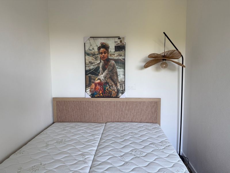 Bedroom in a studio apartment with a picture above the bed and a hanging lamp.