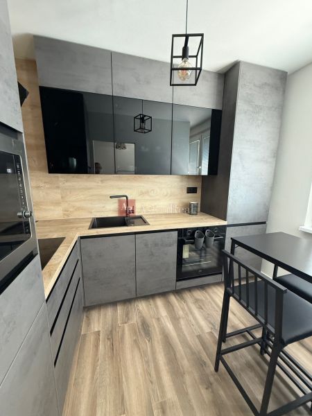 A kitchen with black and gray cabinets, a wood-patterned floor, and a dining table in a studio apartment.