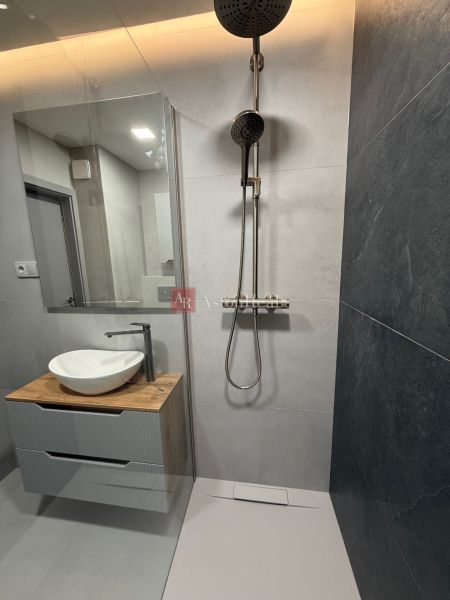A bathroom with a sink on a wooden decor and a shower in a studio apartment.