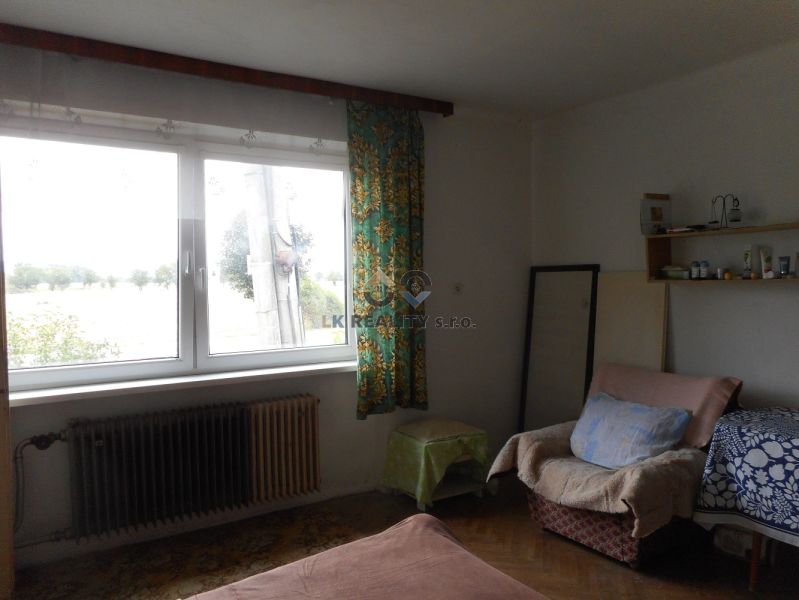 Interior of a family house with an armchair, bed, shelf, and large window.