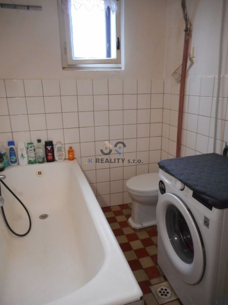 A family house bathroom with a bathtub, a washing machine, and tiles on the wall.