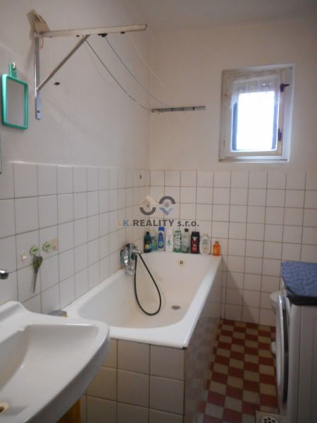 A bathroom in a family house with a bathtub, a washing machine, and a window.