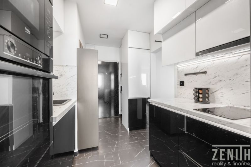 A kitchen in a 2-room apartment with black and white cabinets and marble tiles.