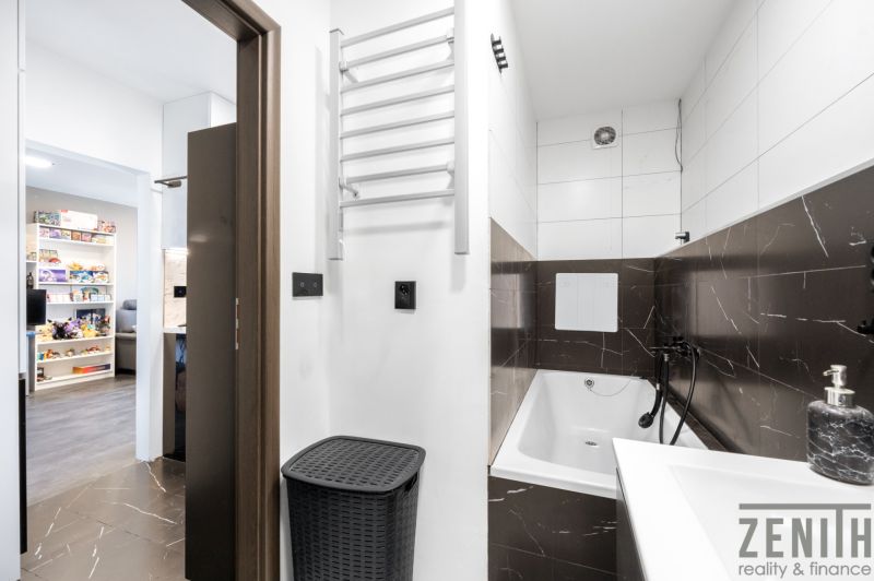 A bathroom in a 2-room apartment with a bathtub and dark tiles.