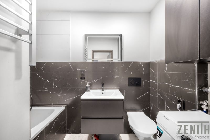 Bathroom with a shower, dark tiles, and a mirror in a 2-room apartment.