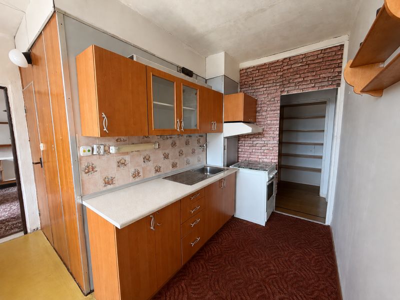 A kitchen in a 3-room apartment with tiles, a kitchen unit, and a brick-patterned wallpaper.
