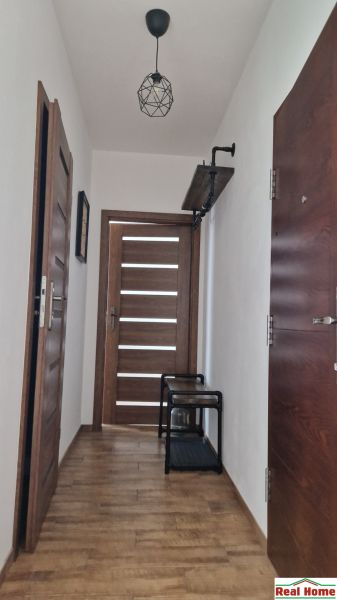 A hallway with a wooden decor floor in a 2-room apartment, doors, and a coat rack shelf.