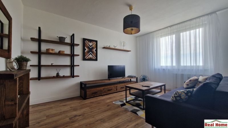 Living room in a 2-room apartment with a sofa, TV, shelves, and a floor with a wooden decor.