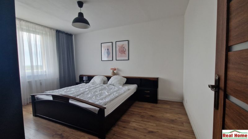 A bedroom in a two-room apartment with a wooden decor floor, a bed, and pictures on the wall.