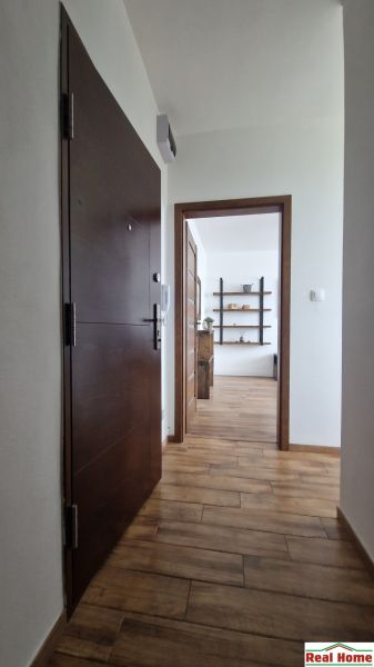A hallway with a wood-patterned floor leading to a room with shelves in a 2-room apartment.