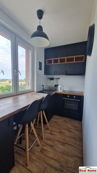 A kitchen in a 2-room apartment with a wooden decor floor, black cabinets, view from the window.
