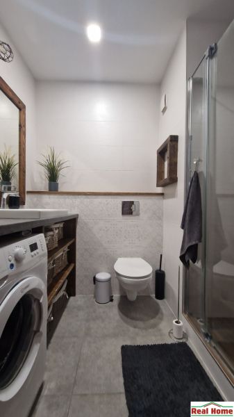 A bathroom in a 2-room apartment with a washing machine, shower, and gray tiles.