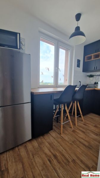 The kitchen of a 2-room apartment with a wooden decor floor, bar stools, and a window.