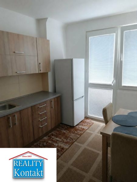 A kitchen in a 2-room apartment with a wooden decor floor and a table with chairs.
