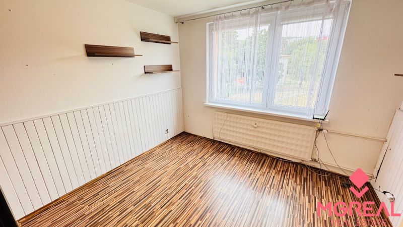 A room with a wooden decor floor, shelves, and a large window in a 3-room apartment.
