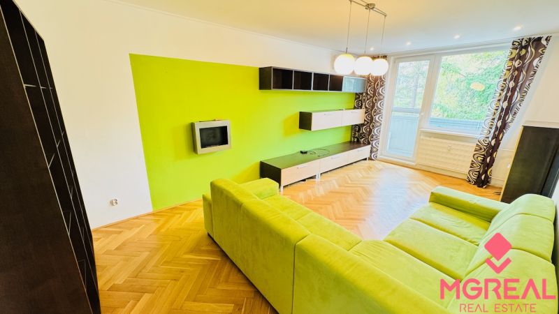Living room with a colorful wall, green sofa, and wooden decor flooring.