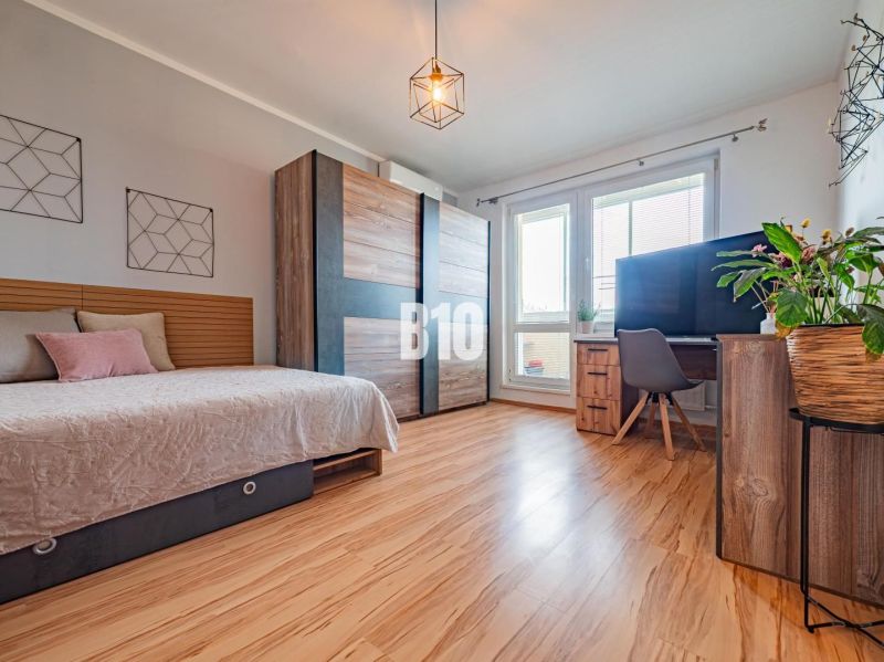 1-bedroom apartment with a bed, large window, TV, wall decorations, and a floor with a wooden design.