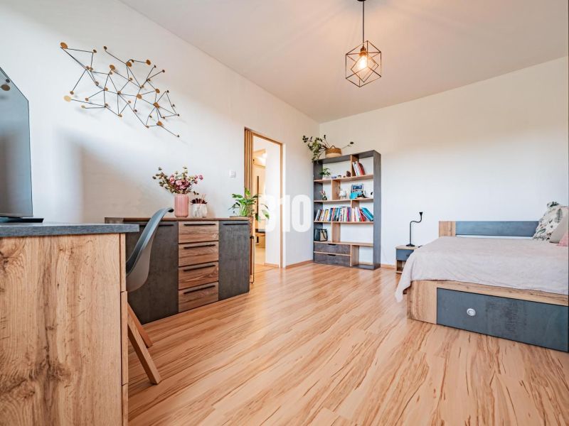 A one-room apartment with a wooden decor floor, a work desk, and a cozy bed.
