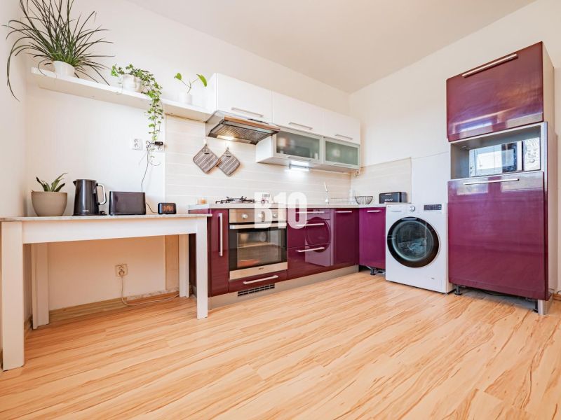 A kitchen with white shelves, a modern countertop, and a wooden decor floor in a studio apartment.