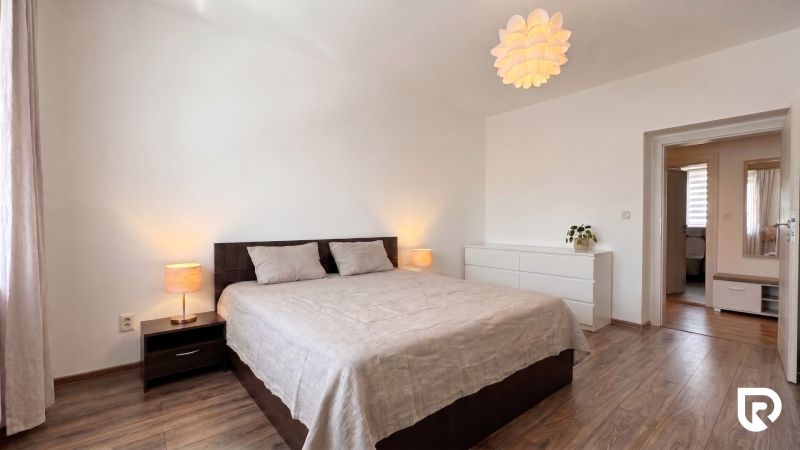 Bedroom in a 2-room apartment with a bed, dresser, and wooden decor flooring.