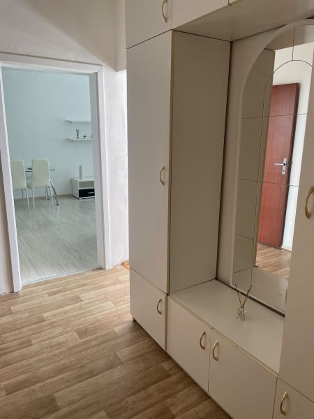 Studio apartment with white furniture and wood-patterned flooring, complemented by a mirror.