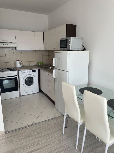 A kitchen in a studio apartment with a kitchenette, refrigerator, and wooden decor flooring.