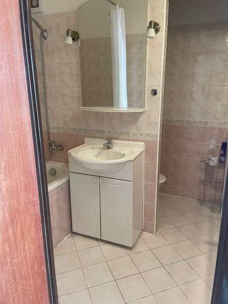 A bathroom in a studio apartment with a sink, bathtub, and ceramic tiles.