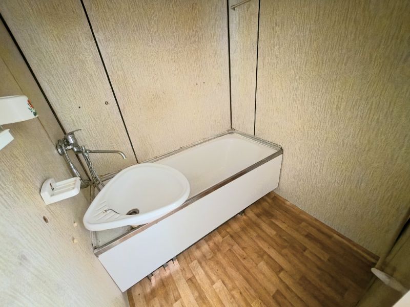 A bathroom in a studio apartment with a bathtub and a wooden decor floor.