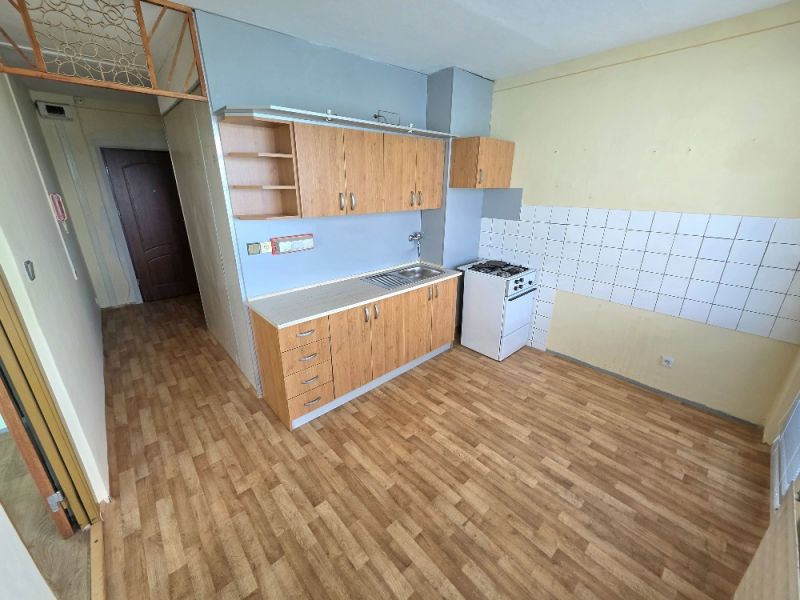 A kitchen in a studio apartment with a wood-patterned floor and basic equipment.