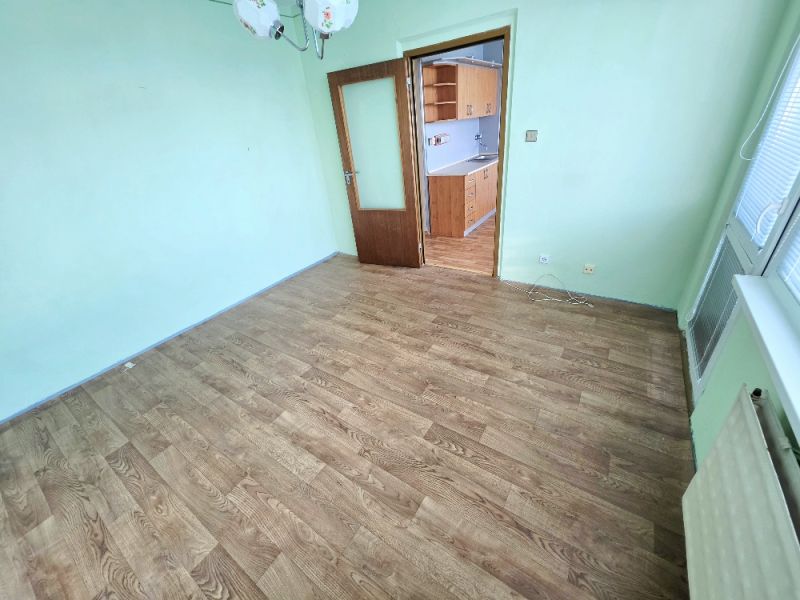 A room in a one-room apartment with a wooden decor floor and a transition to the kitchen.