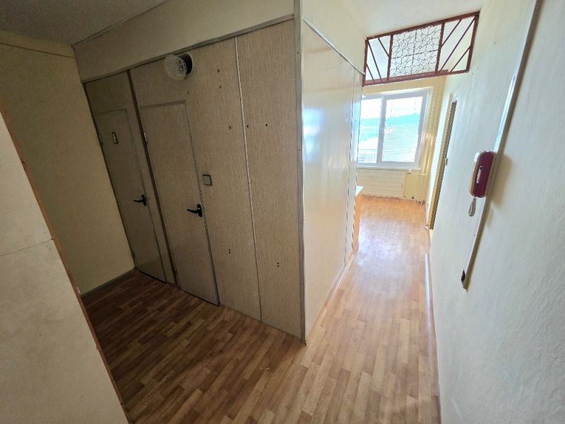 A hallway in a one-room apartment with a wooden decor floor, built-in wardrobes, and a window.