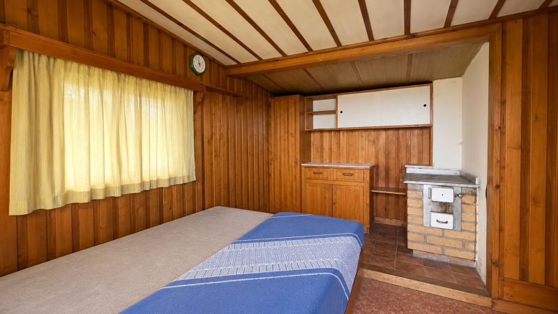 Wooden interior with a bed, stove, and curtains in the garden.