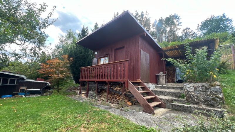 A wooden cottage in the Gardens of Ružomberok surrounded by greenery and trees on a slope.