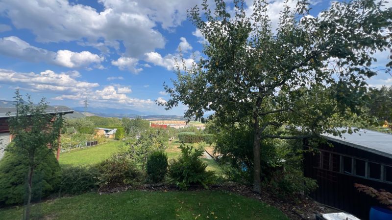 Gardens in Ružomberok with a view of the mountains, with trees and cottages under a blue sky.
