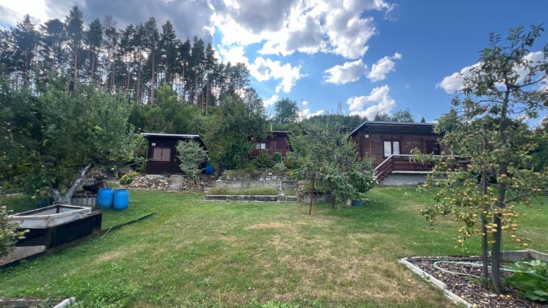 Cottages surrounded by greenery in gardens in Ružomberok under a blue sky with clouds.