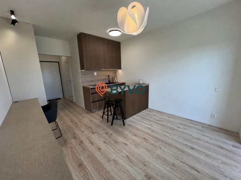 Studio apartment with a kitchenette, counter, and wooden decor flooring.