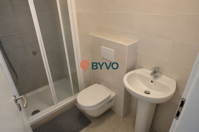 A bathroom in a studio apartment with a white sink, shower stall, and wall-mounted toilet.