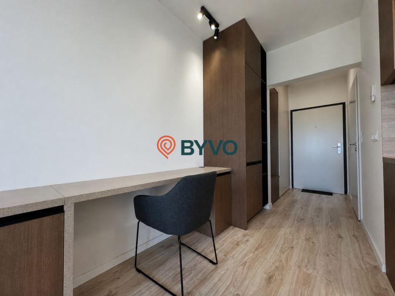Studio apartment with a workspace, chair, and wood-patterned flooring, equipped with storage spaces.