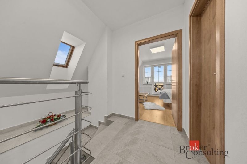 Hallway with a staircase and doors leading to a room with wood-patterned flooring.
