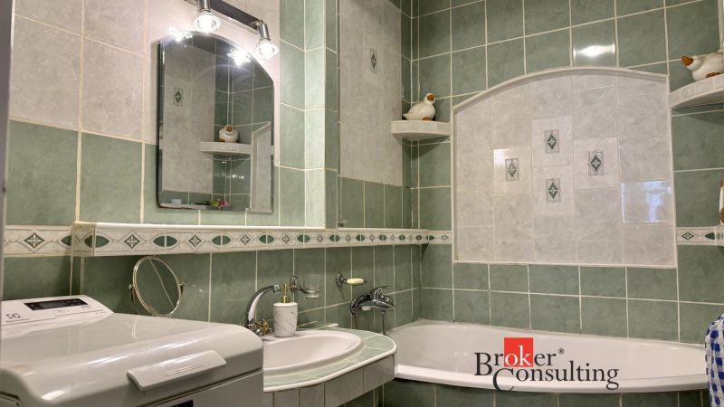A bathroom in a 3-room apartment with a washing machine, sink, and green tiles.