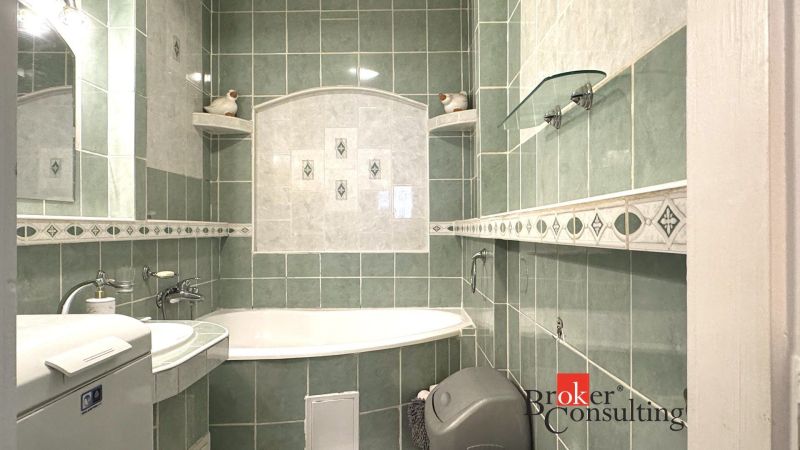 A bathroom with green tiles, a bathtub, and a washing machine in a 3-room apartment.
