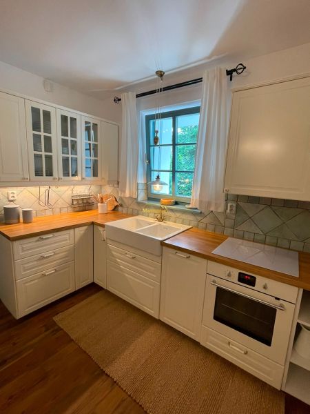 A kitchen in a family house with white cabinets, wooden decor, and a blue window.