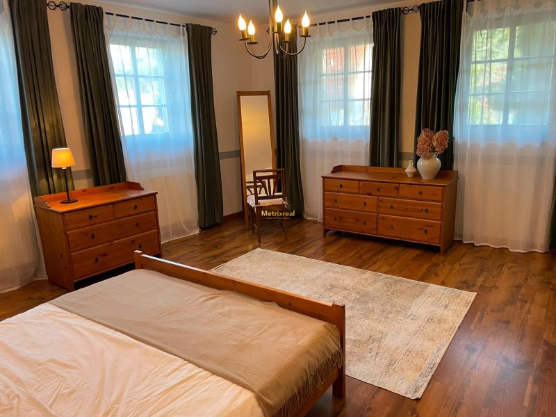 A bedroom with wooden furniture, a floor with a wooden decor, and large windows in a family house.