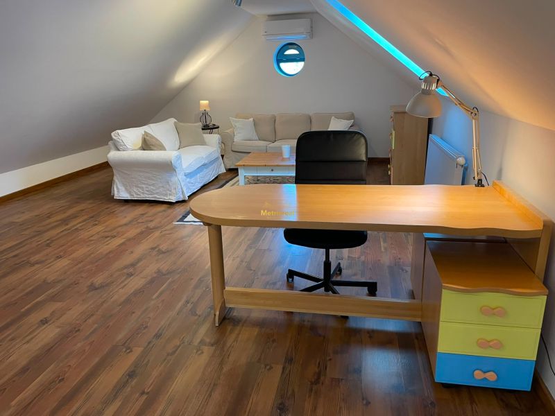 Attic space with a desk, sofa, and wooden decor flooring in a family house.